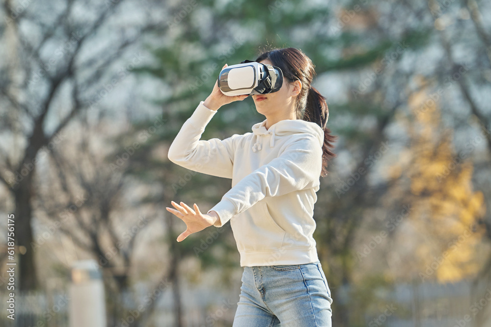 Young college student female model wearing 3D glasses and experiencing virtual reality in an outdoor autumn lawn plaza at a university in South Korea, Asia.