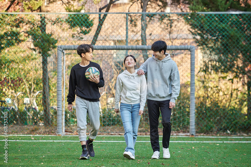 Three young male and female college models walk with a ball and raise their hands in celebration after a game at a fall college futsal field in South Korea, Asia. 