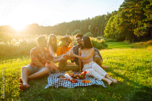 Group of young people having fun while drinking beer, talking at picnic party outside city on warm summer day. Vacation, picnic, friendship or holliday concept.