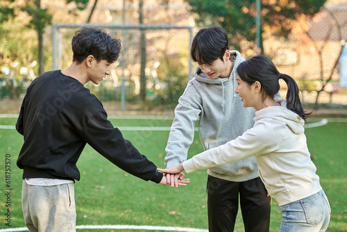 Three young male and female college models walk with a ball and raise their hands in celebration after a game at a fall college futsal field in South Korea, Asia. 
