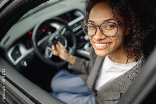 Foto Young smiling woman holding keys to rental car before trip and smiling at camera