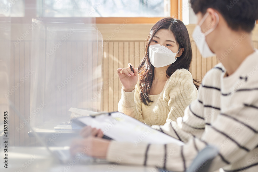 Obraz premium Young Asian college and university students, male and female models, studying or discussing in class while wearing masks in a university classroom during the Asian Korean Pandemic.