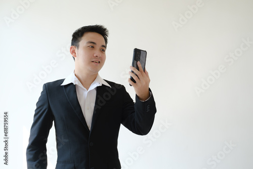 Young Asian businessman with an unpleasant facial expression doing a video call on his smartphone. Isolated white background. Suitable for advertisement.