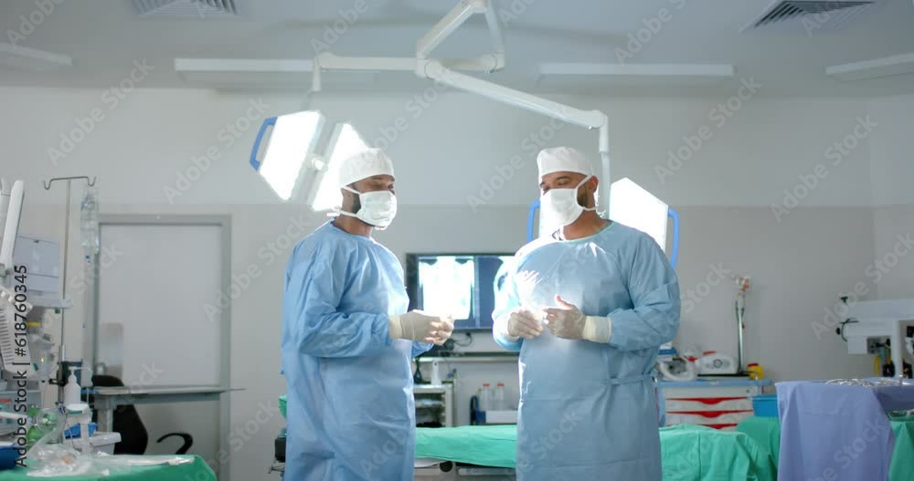 Portrait of diverse male surgeons wearing surgical gowns in operating theatre, slow motion