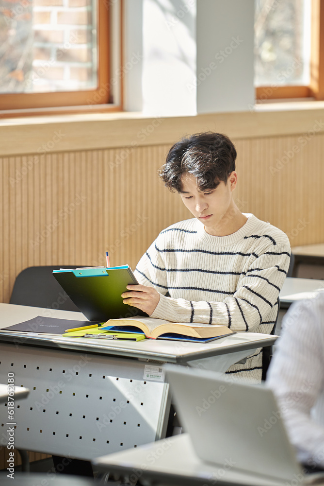 In a higher education classroom in South Korea, young university students are listening to a lecture, studying, and talking. A woman and a man are in the background In a higher education classroom in South Korea, young university students are listening to a lecture, studying, and talking. A woman and a man are in the background