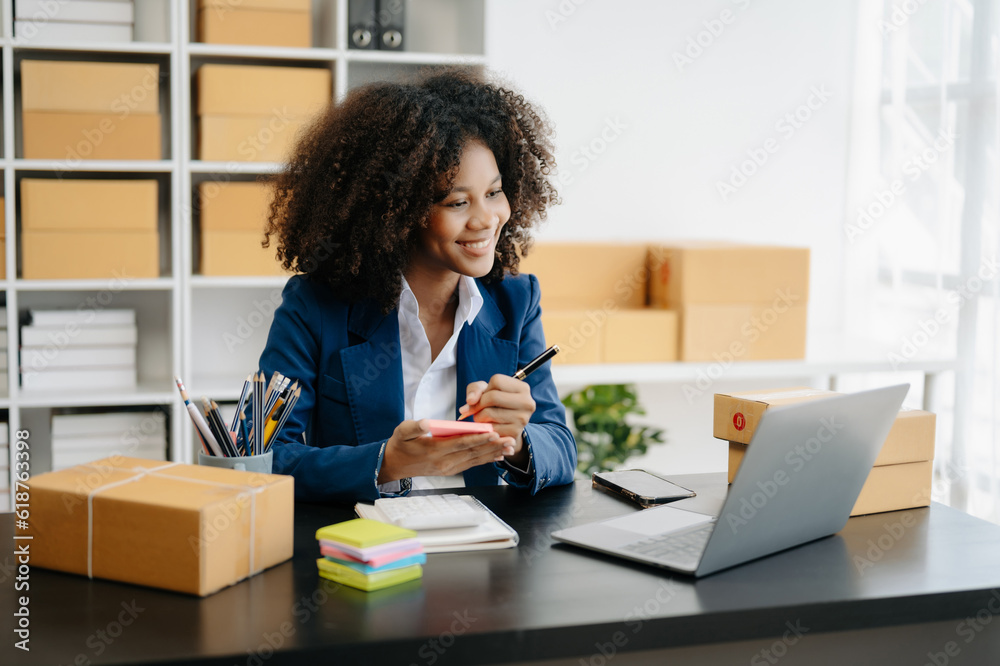 Startup small business SME, Entrepreneur owner African woman using smartphone or tablet taking receive and checking online purchase shopping order to preparing pack product box. . Startup small business SME, Entrepreneur owner African woman using smartphone or tablet taking receive and checking online purchase shopping order to preparing pack product box. .
