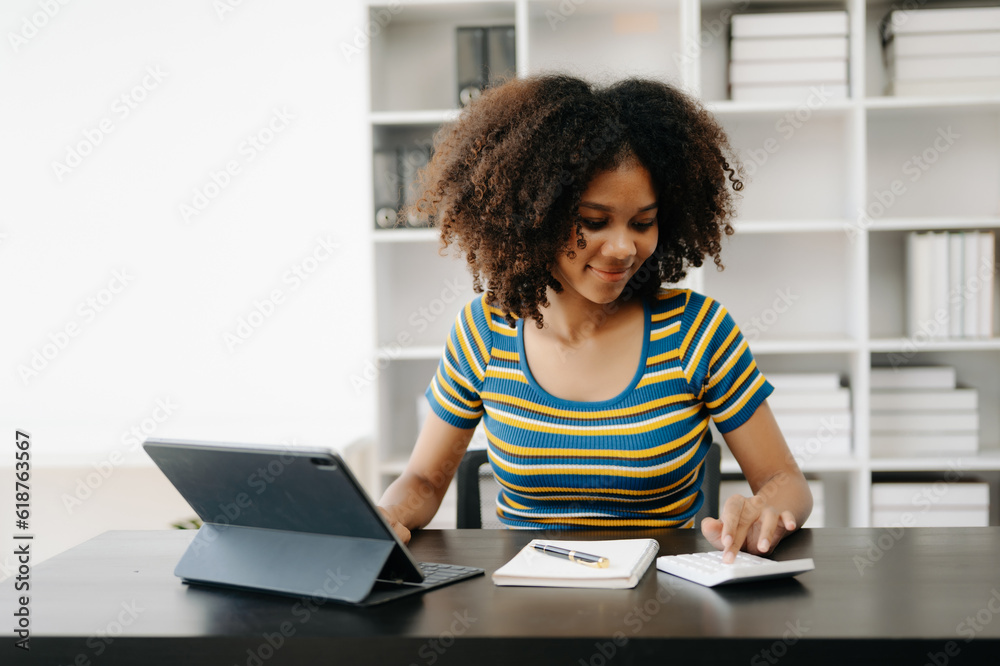 Beautiful African woman using laptop and tablet while sitting at her working place. Concentrated at work in home office Beautiful African woman using laptop and tablet while sitting at her working place. Concentrated at work in home office