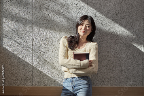 A young female college student model leaning against the wall of a university classroom in a light-filled room in South Korea, Asia.  