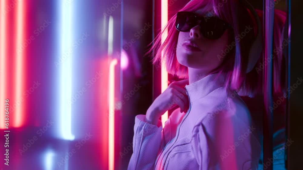 Beautiful woman with purple hair in futuristic costume over dark background. Violet neon light. Portrait of young girl in modern headphones listening music.