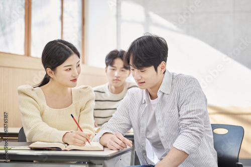 Three young male and female college students models sitting or standing at desks in a university classroom in South Korea, Asia, talking or having a discussion