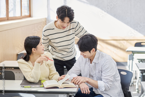 Three young male and female college students models sitting or standing at desks in a university classroom in South Korea, Asia, talking or having a discussion © TEAM PRE-LIGHT