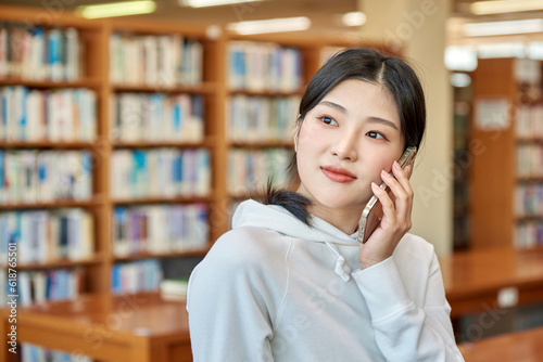 Young Asian Korean female model, male model and bookshelf background looking out the window holding mobile phone in library in library