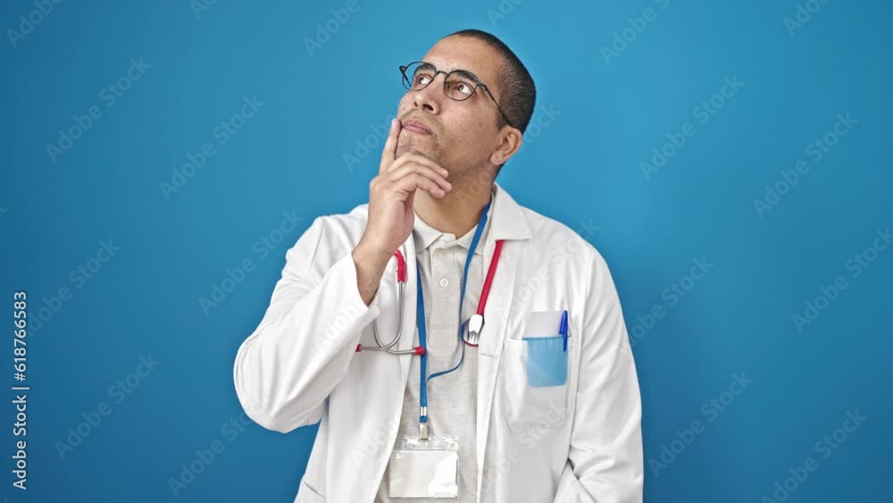 Young hispanic man doctor standing with doubt expression thinking over isolated blue background Young hispanic man doctor standing with doubt expression thinking over isolated blue background