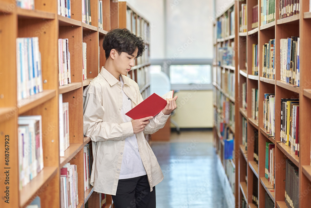 Young variously facial expression male college student model looking for and reading a book on a shelf in a university library in Asia South Korea Young variously facial expression male college student model looking for and reading a book on a shelf in a university library in Asia South Korea