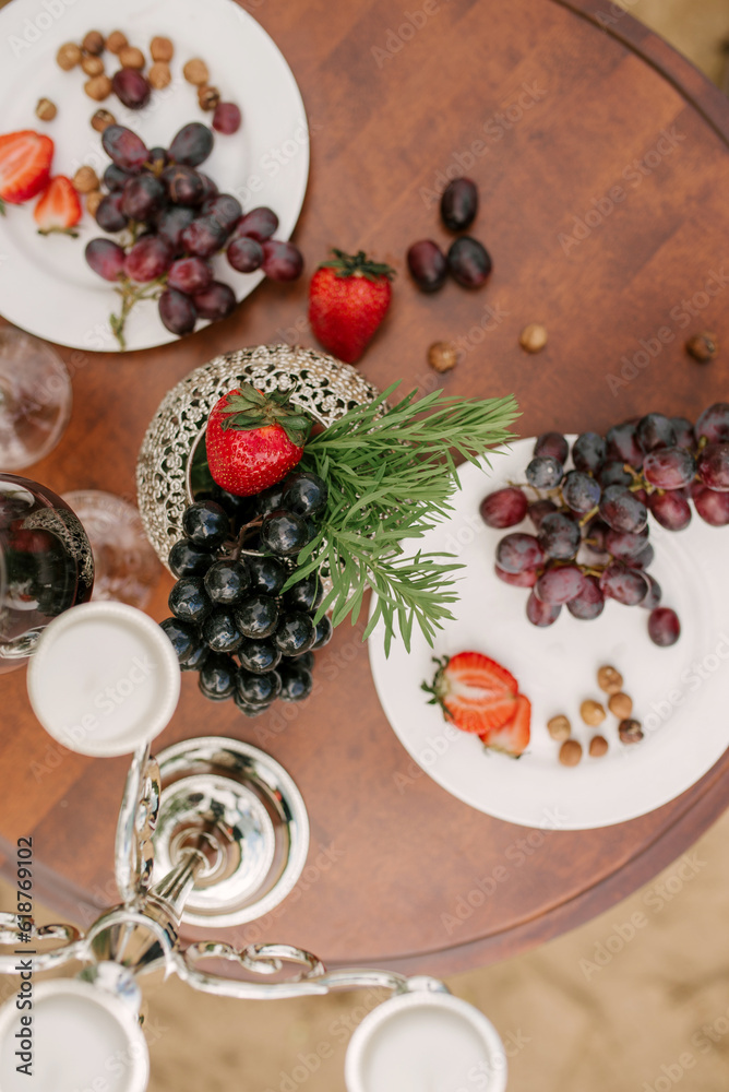 Grapes and strawberries on white plates and scattered on a wooden round table. Top view
