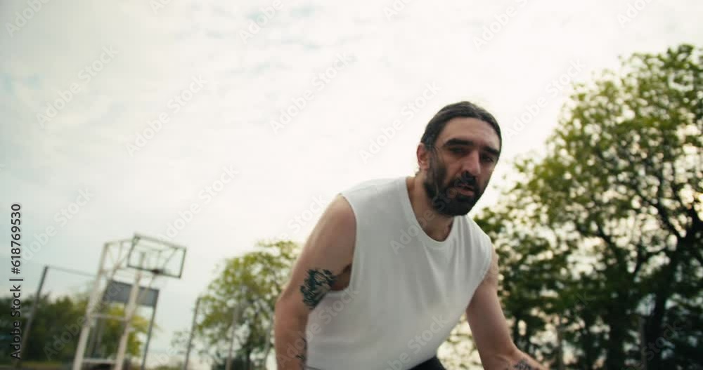 A man in a white T-shirt with a beard skillfully dribbles the ball on the basketball court. Dynamic one player basketball game A man in a white T-shirt with a beard skillfully dribbles the ball on the basketball court. Dynamic one player basketball game