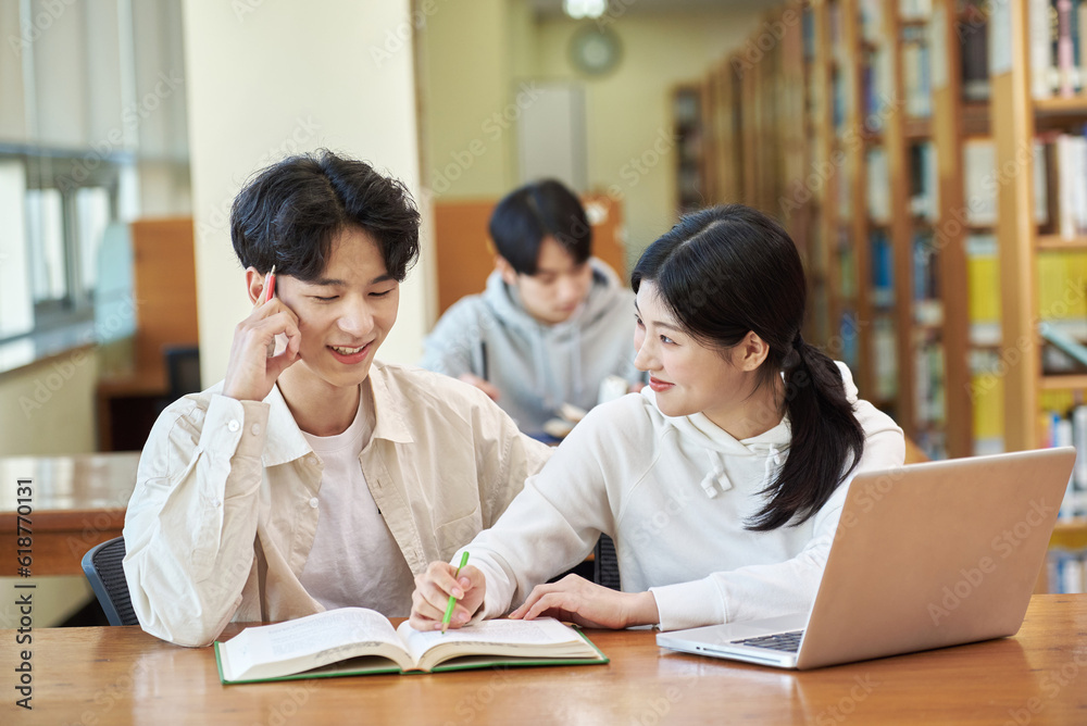 Two young college student man and woman couple model and solo male model looking at laptop and book together in library of Asian Korean university Two young college student man and woman couple model and solo male model looking at laptop and book together in library of Asian Korean university