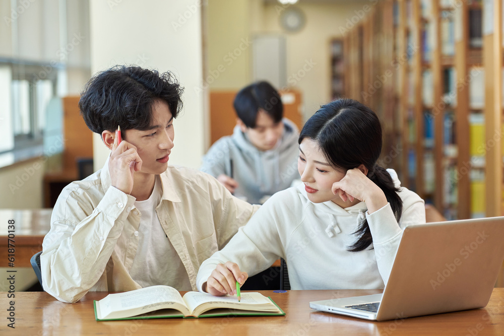 Two young college student man and woman couple model and solo male model looking at laptop and book together in library of Asian Korean university Two young college student man and woman couple model and solo male model looking at laptop and book together in library of Asian Korean university