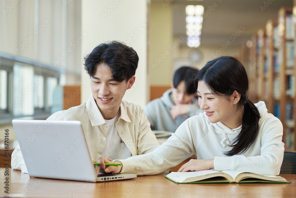 Two young college student man and woman couple model and solo male model looking at laptop and book together in library of Asian Korean university