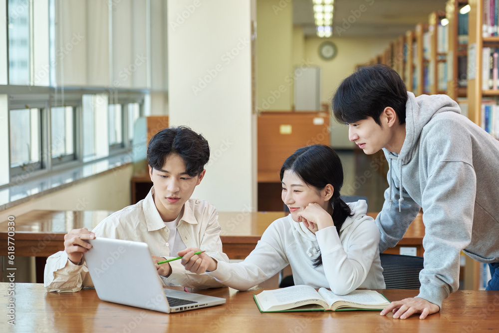 Two young college student man and woman couple model and solo male model looking at laptop and book together in library of Asian Korean university Two young college student man and woman couple model and solo male model looking at laptop and book together in library of Asian Korean university