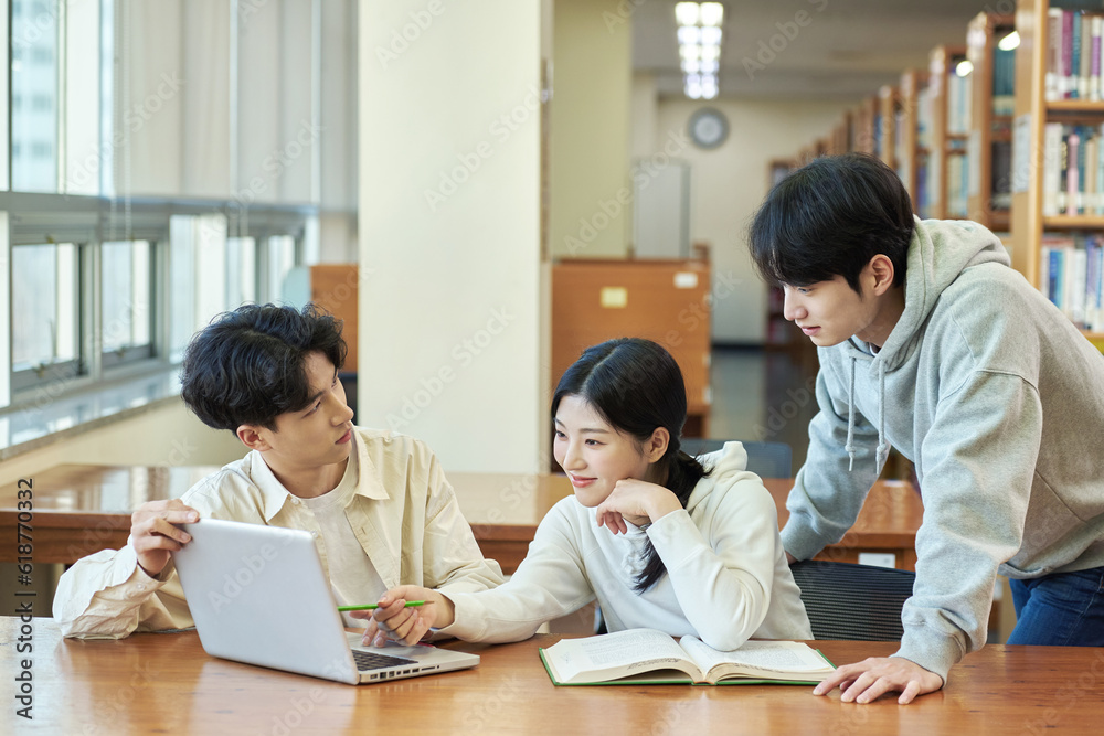 Two young college student man and woman couple model and solo male model looking at laptop and book together in library of Asian Korean university Two young college student man and woman couple model and solo male model looking at laptop and book together in library of Asian Korean university