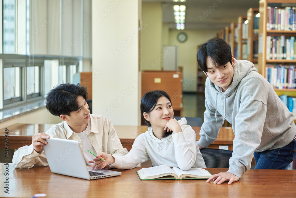 Two young college student man and woman couple model and solo male model looking at laptop and book together in library of Asian Korean university Two young college student man and woman couple model and solo male model looking at laptop and book together in library of Asian Korean university