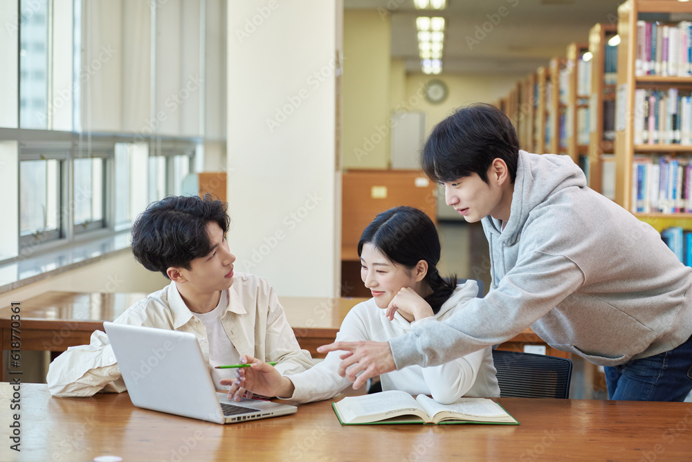 Two young college student man and woman couple model and solo male model looking at laptop and book together in library of Asian Korean university Two young college student man and woman couple model and solo male model looking at laptop and book together in library of Asian Korean university