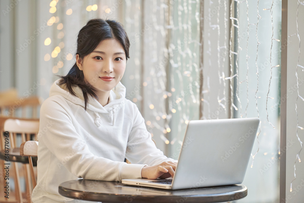 Young female college student model sitting at a cafe table in Asian Korea, listening to a lecture, doing homework or working on a laptop with twinkling lights in the background Young female college student model sitting at a cafe table in Asian Korea, listening to a lecture, doing homework or working on a laptop with twinkling lights in the background