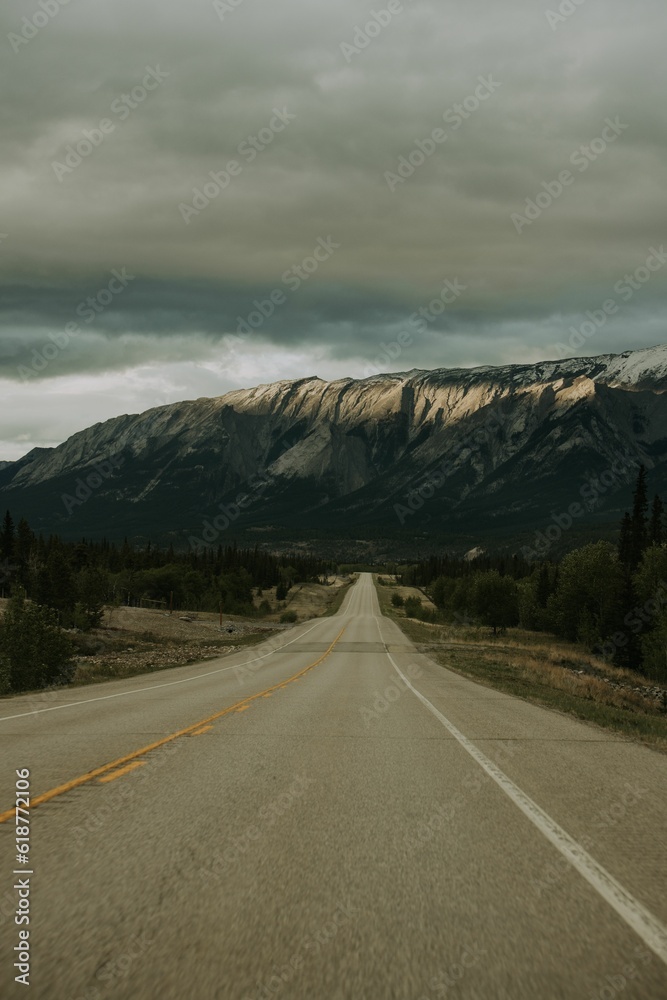 Winding road stretches through a mountainous landscape, with towering peaks and ominous clouds