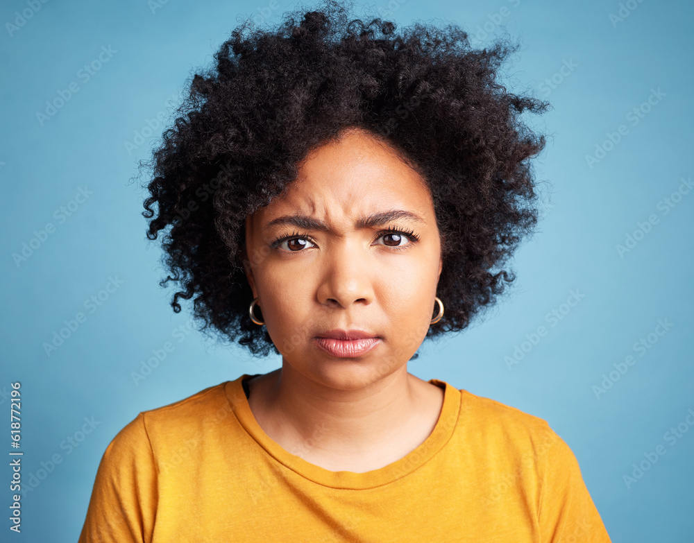 Portrait, frown and anger with an african woman on a blue background in studio looking mad or serious. Face, bad or negative and an unhappy young female person with an afro feeling frustrated Portrait, frown and anger with an african woman on a blue background in studio looking mad or serious. Face, bad or negative and an unhappy young female person with an afro feeling frustrated