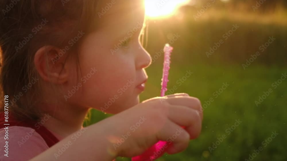 Close-up of cute little child girl inflates soap bubbles at amazing summer sunset. Childhood dream concept. Transparent soap balls flying air ray sunlight. Pretty daughter playing game. Slow motion Close-up of cute little child girl inflates soap bubbles at amazing summer sunset. Childhood dream concept. Transparent soap balls flying air ray sunlight. Pretty daughter playing game. Slow motion
