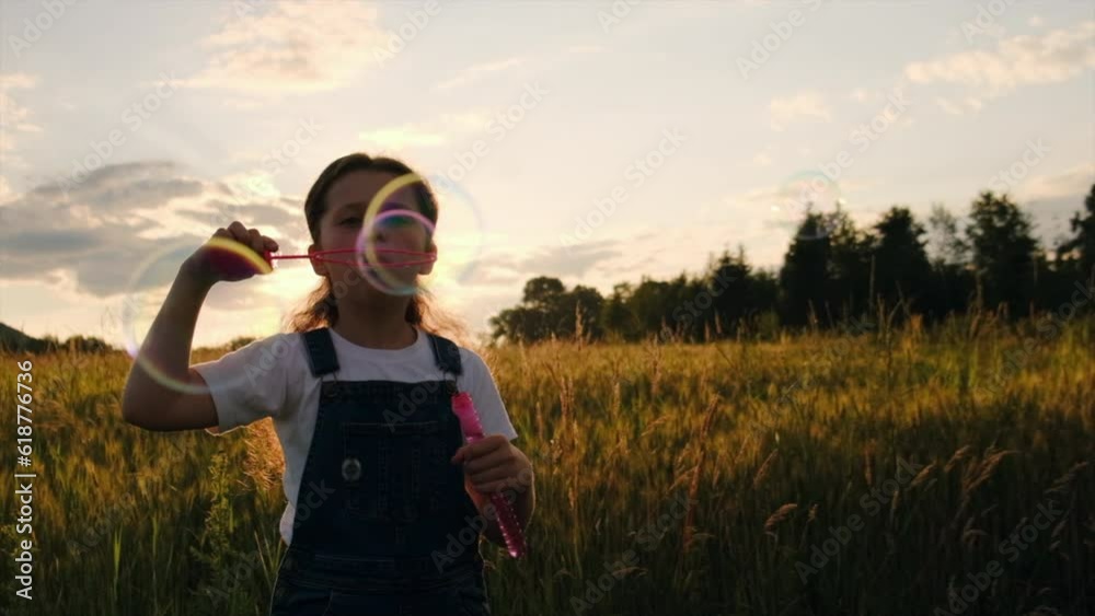 Silhouette of preteen girl blowing soap bubbles, having fun playing on field at amazing sunset. Child plays with soap bubbles in nature. Happy childhood concept. Playful kid enjoy weekend. Slow motion Silhouette of preteen girl blowing soap bubbles, having fun playing on field at amazing sunset. Child plays with soap bubbles in nature. Happy childhood concept. Playful kid enjoy weekend. Slow motion