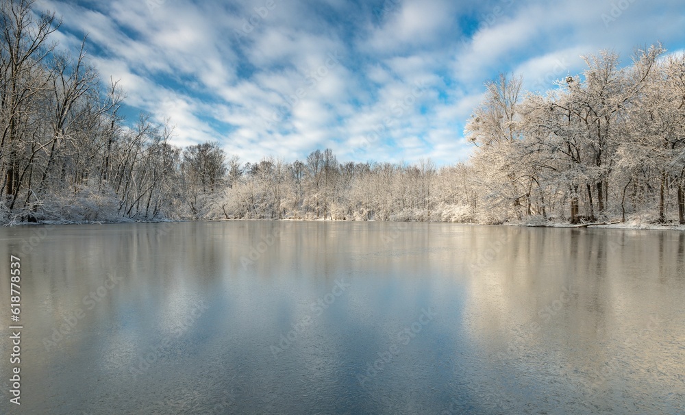 Landscape of a frozen lake surrounded by trees and snow under a blue cloudy sky Landscape of a frozen lake surrounded by trees and snow under a blue cloudy sky