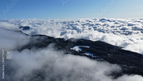 Stunning view of the clouds over the mountains covered in dense trees at sunlight
