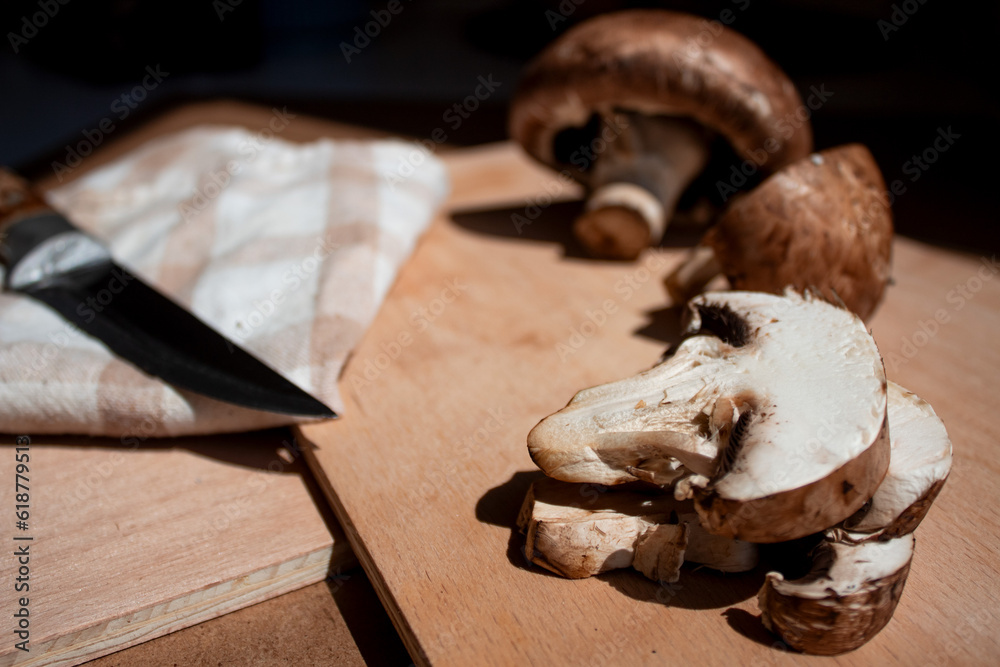 mushrooms (large champignons with a brown cap) lie on a wooden board, one mushroom is cut and the other is whole, a knife and a kitchen towel are next to it mushrooms (large champignons with a brown cap) lie on a wooden board, one mushroom is cut and the other is whole, a knife and a kitchen towel are next to it