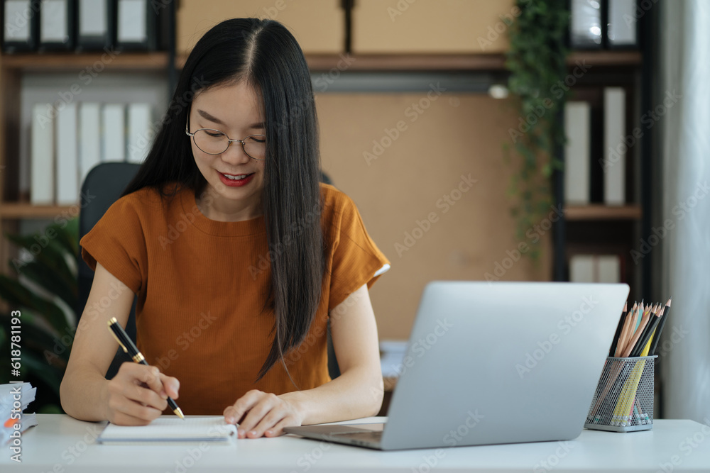Woman using laptop to work and writing on notebook with pen in home office with mobile next to laptop. Woman using laptop to work and writing on notebook with pen in home office with mobile next to laptop.