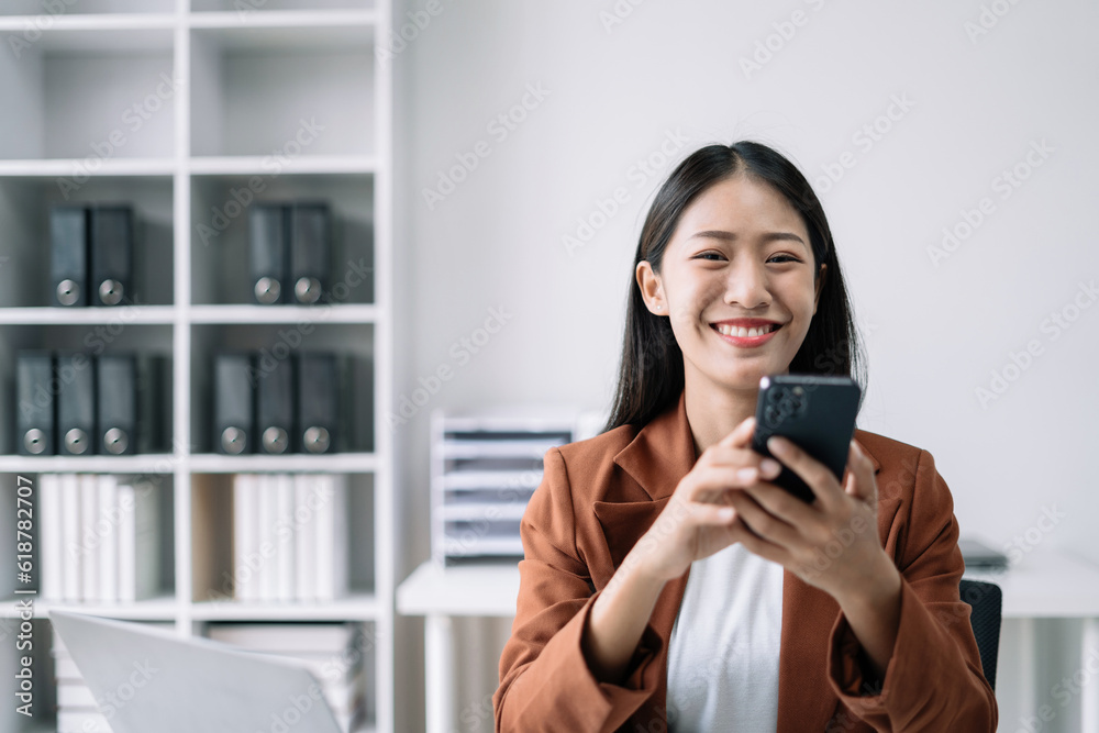 Female asian woman holding smartphone sitting at the desk, looking to camera. Female asian woman holding smartphone sitting at the desk, looking to camera.