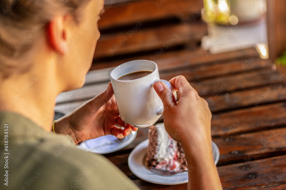 An unrecognizable female person enjoying a first sip of coffe and a piece of cake at a rustic outdoor dining space in summer An unrecognizable female person enjoying a first sip of coffe and a piece of cake at a rustic outdoor dining space in summer