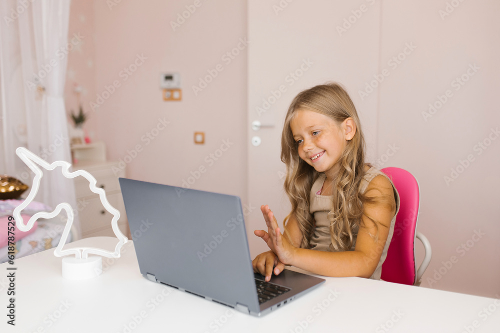 Girl sitting at her desk looks at the laptop screen and types on the keyboard