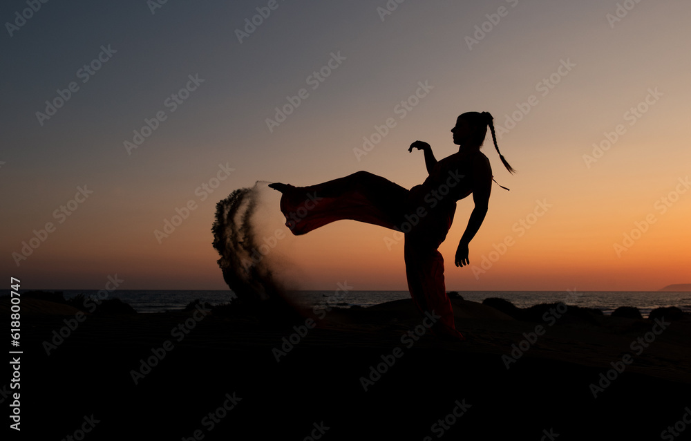 Silhouette of a woman dancing at a sandy beach at sunset. Caucasian woman posing outdoors at the coast