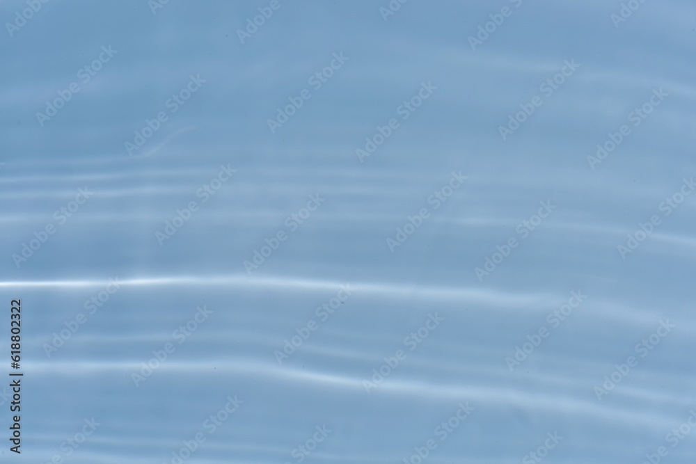 Blue water with ripples on the surface. Defocus blurred transparent blue colored clear calm water surface texture with splashes and bubbles. Water waves with shining pattern texture background.