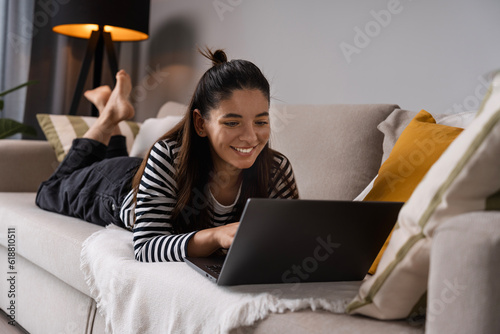 Relaxed study. Attractive student lying on sofa bed cheerfully working on laptop