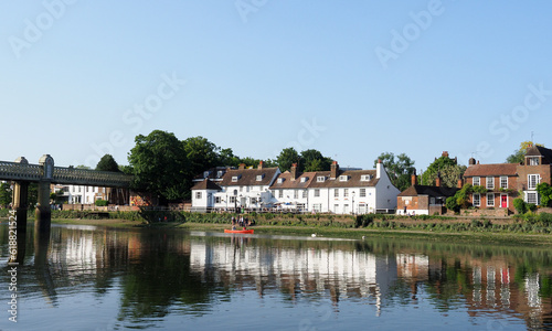 Tranquil evening scene on the River Thames with a red canoe passing a whitewashed pub © chris