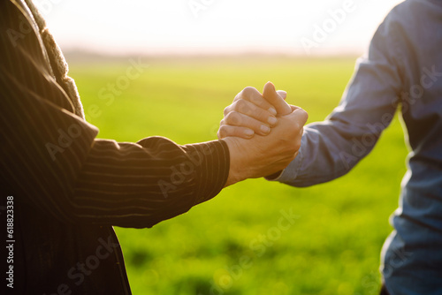 Fototapeta Two farmers shake hands after a fraction in a green wheat field