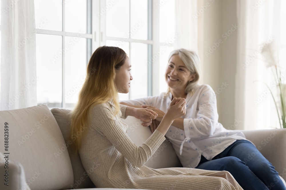 Happy mature grandma talking to teenage grandkid girl, sitting on couch, listening to speaking kid, smiling, laughing, enjoying conversation, trust, friendship, family relationship