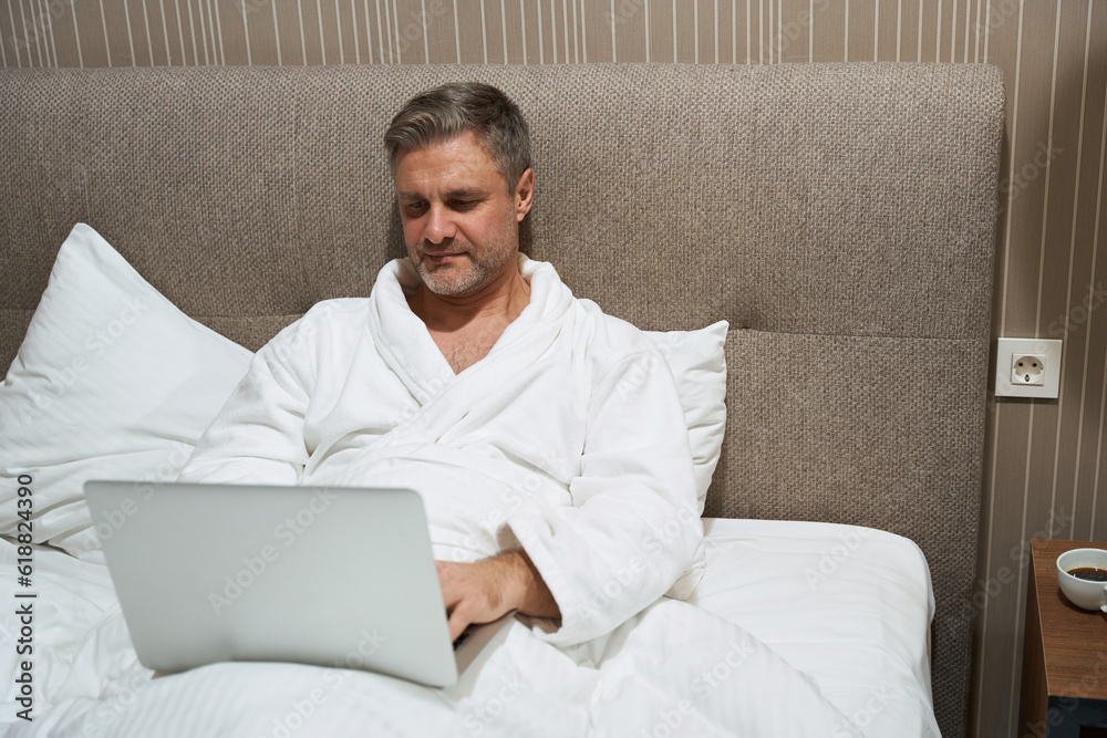 Man resting on bed and typing on computer Man resting on bed and typing on computer