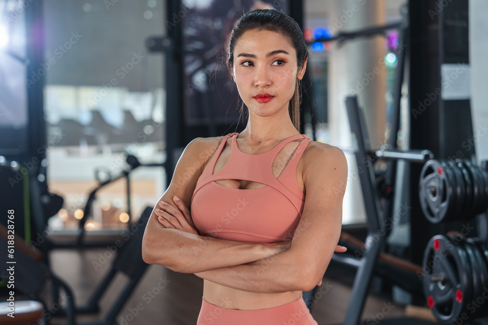 Fitness healthy Asian woman standing with arms crossed, muscular body in gym sport club.