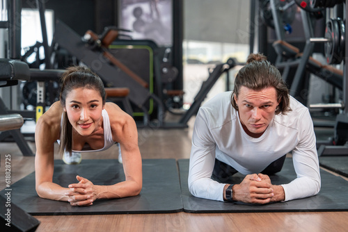 Healthy lifestyle and fitness concept. Asian woman wearing sports bra doing plank exercise together with caucasian male trainer building strength in sport gym