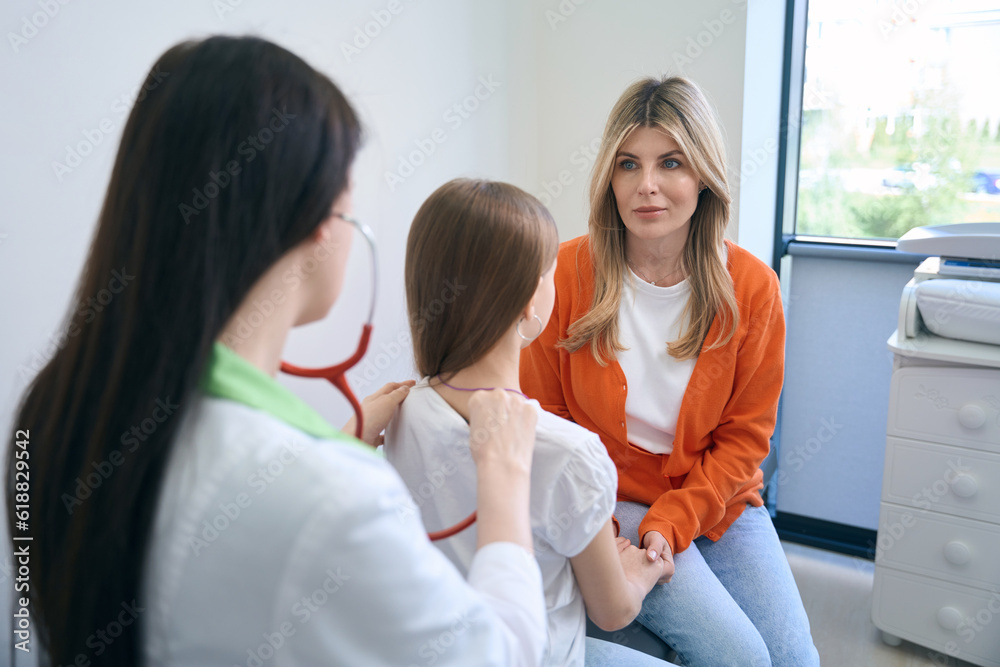 Obraz premium Pediatrician attentively listening to little girl lungs using stethoscope