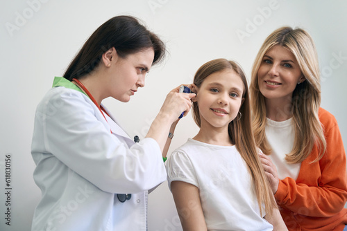 Concentrated woman laryngologist examining ear of little patient with otoscope